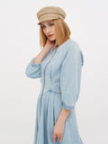 Woman touching beige linen baker boy cap, side view, blue linen dress