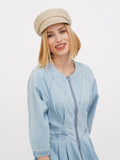 Close-up of woman touching beige linen baker boy cap, smiling
