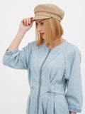 Woman in beige linen Breton cap shielding eyes, side angle, blue dress