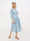 Close-up of woman in beige linen newsboy cap looking down, blue dress