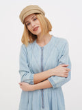 Woman wearing beige linen newsboy cap with arms crossed, front view