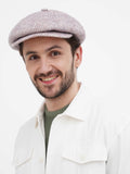 Close-up front torso view of man wearing beige slouchy newsboy cap smiling