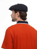 Back view of man wearing black newsboy cap showing 8-panel construction and orange shirt detail