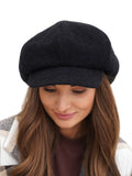 Angled portrait of woman in black cashmere baker boy cap white background