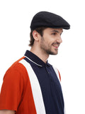 Black flat top newsboy cap side profile view showing sleek construction with polo shirt