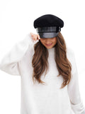 Woman in white sweater wearing black cashmere Breton cap with lacquered visor