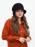 Close-up of woman adjusting black wool cloche hat, wearing rust orange shirt