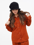 Side view of woman in rust orange outfit wearing black cloche hat, hand near collar
