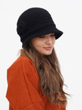Woman in rust orange shirt wearing black cloche hat, side profile close-up