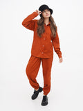 Full-length photo of woman in rust orange outfit wearing black cloche hat, walking pose