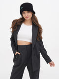 Woman in grey blazer and trousers wearing black cloche hat, adjusting jacket