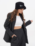 Woman in grey blazer and trousers wearing black cloche hat, adjusting jacket