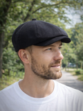 Man in black linen newsboy cap three quarter view outdoor setting