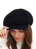 Angled portrait of woman wearing black wool paperboy cap with long hair