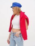 Woman in blue linen baker boy cap pulling on red cardigan, looking down