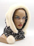 Cream natural mink fur hat hood with black patterned fabric ties and cream pompons on female model, front view