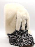 Side profile cream mink fur hat hood on mannequin showing cream pompon at black patterned fabric tie end