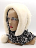 Three-quarter view cream mink fur hat hood showing ivory mink surface and black patterned tie with pompon