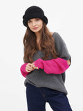 Woman in grey sweater and pink sleeves wearing dark grey cloche hat, arms crossed
