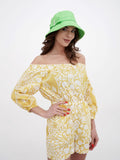 Woman in green sun hat adjusting brim, yellow printed dress