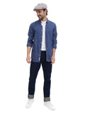 Full body shot man wearing grey 8-panel newsboy cap with blue denim shirt and dark pants