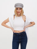 Woman in grey linen newsboy cap with white top and navy jeans, hands on hips