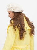 Close-up of ivory wool beret with fabric flower on woman's head showing cream-white color and petal detail