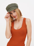 Woman wearing khaki linen newsboy cap with rust ribbed dress, smiling