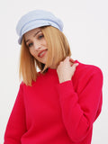 Woman wearing light blue linen Breton cap with red sweater, looking over shoulder