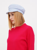 Close-up of woman adjusting light blue linen newsboy cap, red sweater