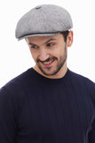 Light grey baker boy hat styled with navy sweater casual standing pose hands in pockets