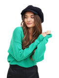 Angled full body view woman in navy wool baker boy cap black skirt green sweater