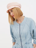 Close-up of woman in peach linen baker boy cap touching face, smiling