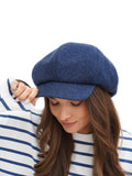 Side profile of woman wearing royal blue wool newsboy cap with long dark hair
