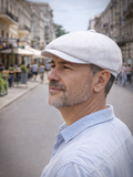 Man wearing white linen newsboy cap side view city blue shirt