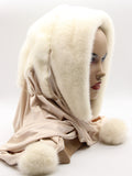 White natural mink fur hat hood with light beige fabric scarf and three white mink pompons on female model, front view